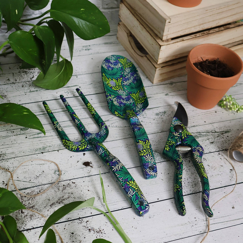 Three gardening tools rest on a table surrounded by vibrant green plants, showcasing a serene gardening scene.