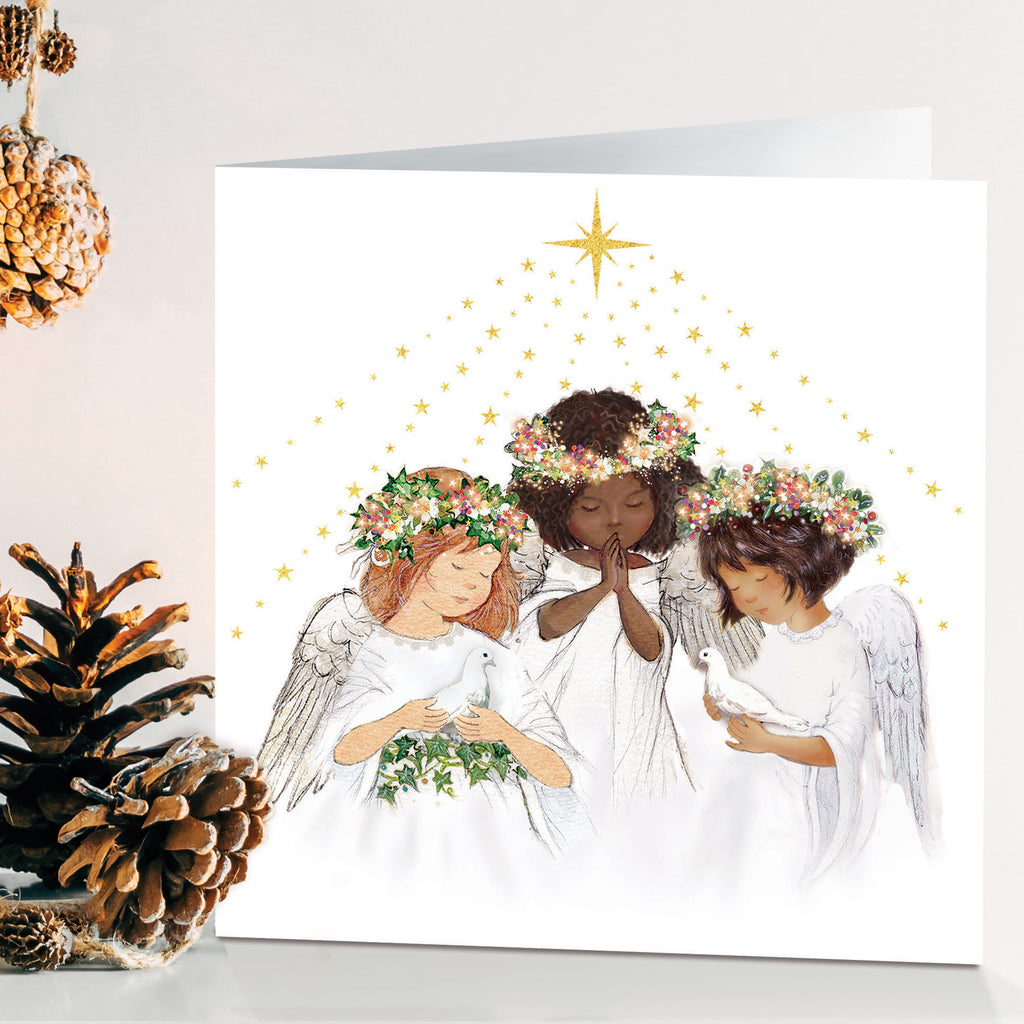 Three girl angels praying under the north star holding doves with a Christmas themed background of snowy pinecones