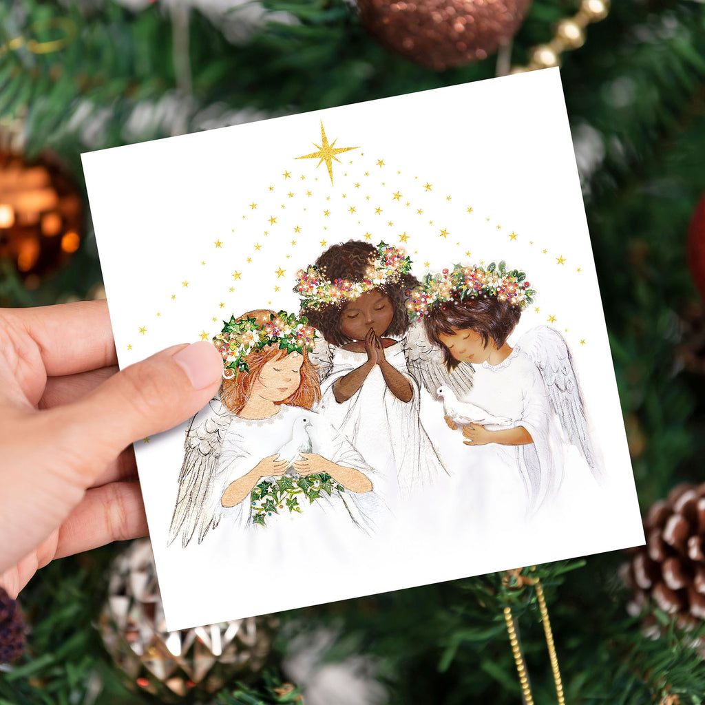 Three girl angels praying underneath the north star holding doves with a backdrop of a festive Christmas Tree 