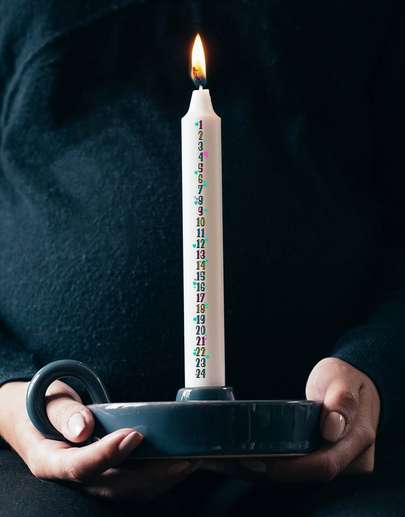 A lit Christmas Advent Candle being held with two hands by an individual wearing a knitted dark coloured jumper.