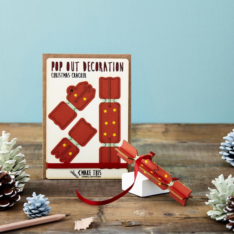 Christmas cracker wooden card tree decoration with red ribbon attached and on a snowy Christmas background