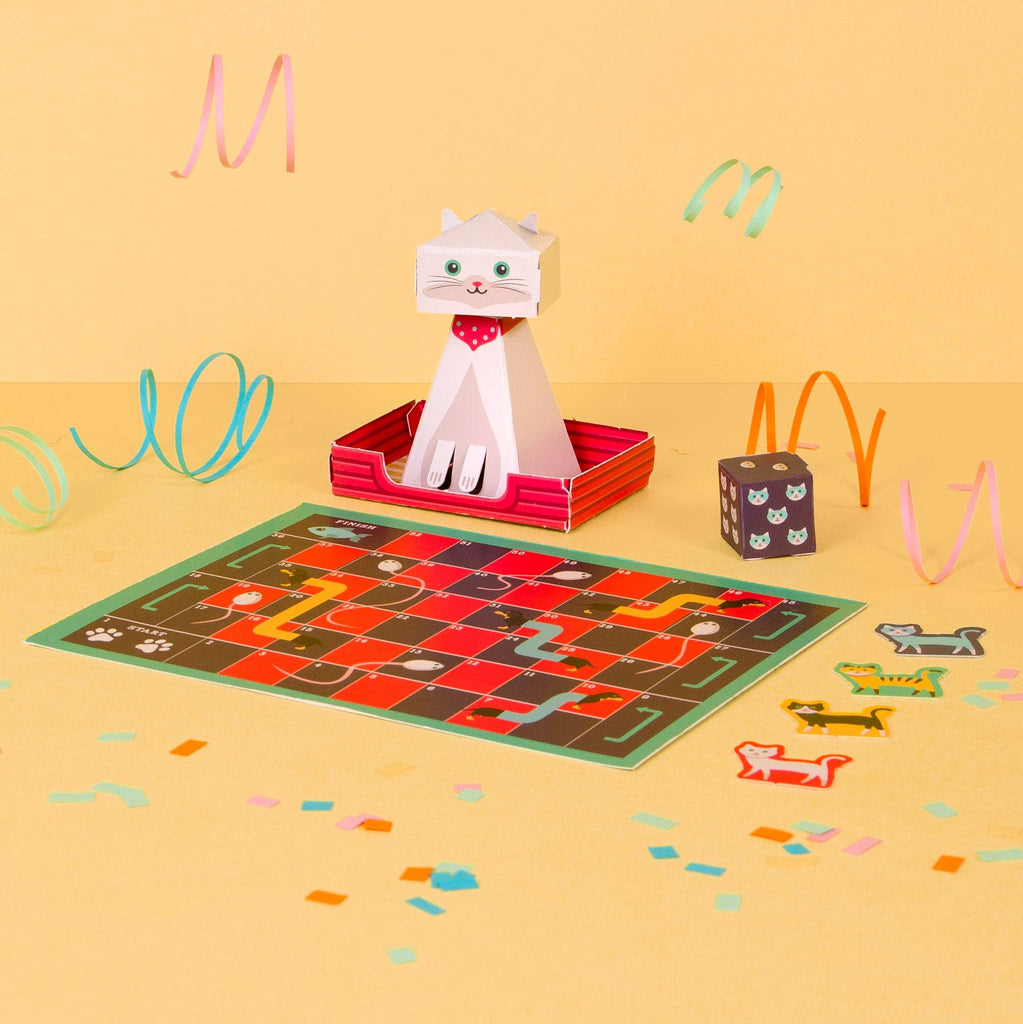 A playful scene featuring a paper cat game surrounded by colourful confetti and various toys scattered around.