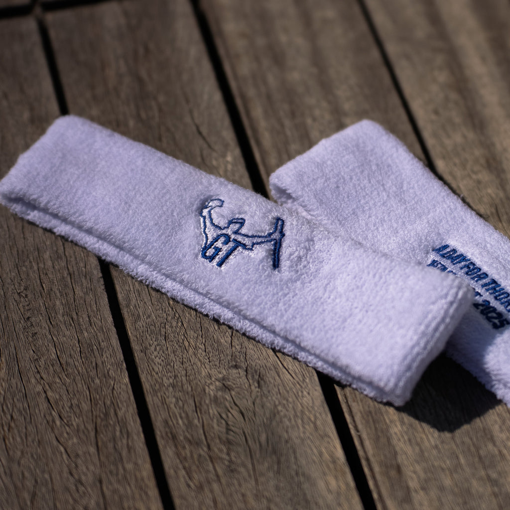 Two white sweatbands with embroidered logos on a wooden surface