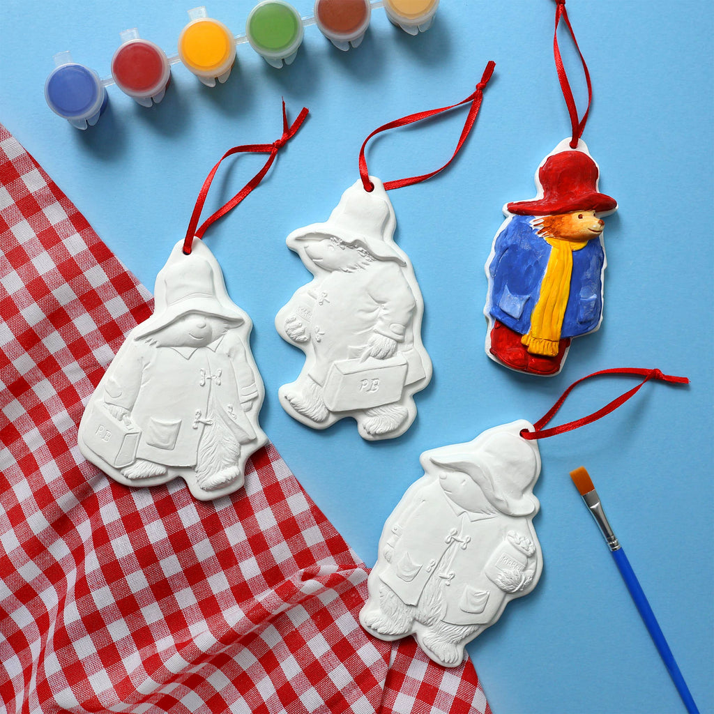 Colourful 4 Paddington Bear Christmas ornaments, surrounded by a brush and pots of paint.