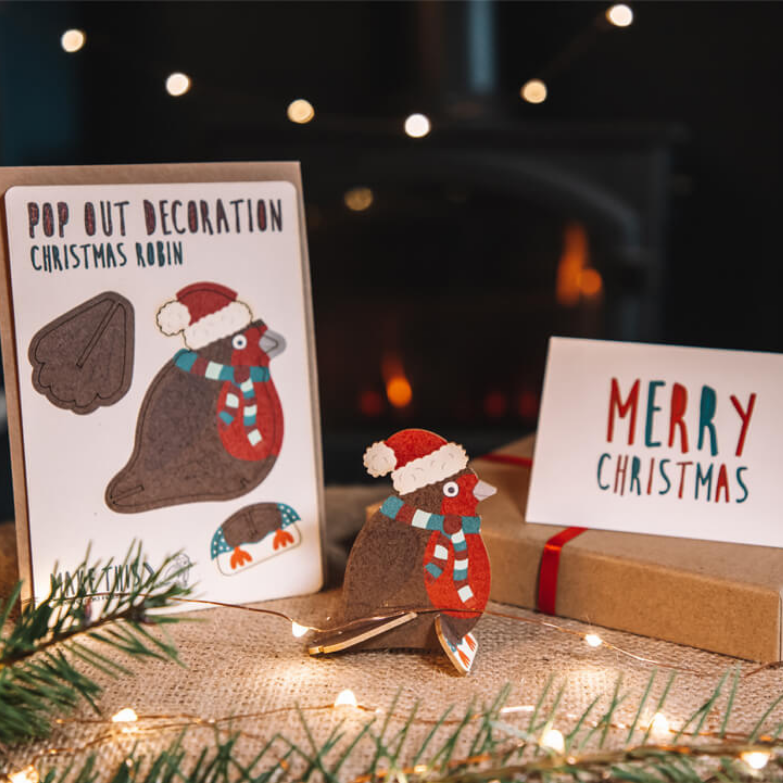 Robin Christmas Card next to festive fireplace and lit Christmas tree