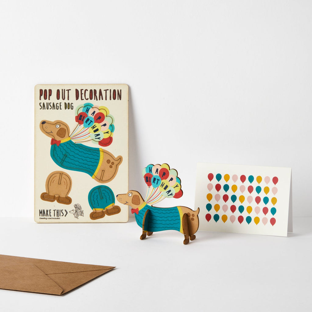 Sausage Dog with blue knitted jumper and red bowtie standing wooden card attached to multi coloured balloons spelling happy birthday