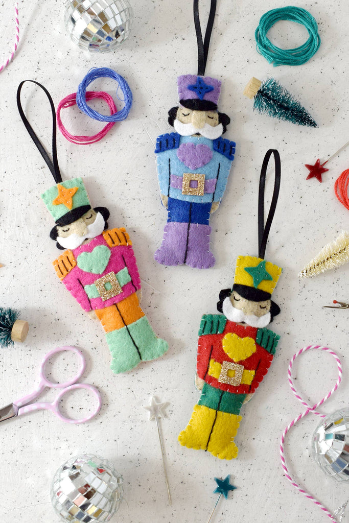 Colorful felt nutcrackers, each uniquely designed, hang from a string, adding charm to the holiday decor.